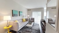 This single-floor residence offers a thoughtfully designed layout with a clean, contemporary aesthetic throughout. The living room serves as the heart of the space, featuring warm hardwood-style flooring, neutral wall tones, and a large sliding glass door fitted with vertical blinds that floods the room with natural light and provides access to an outdoor area with lush green views. The open, airy atmosphere is complemented by tasteful wall art and a comfortable seating arrangement.

The kitchen is efficiently organized with warm-toned wooden cabinetry, grey subway tile backsplash, stainless steel appliances including a gas range, microwave, and refrigerator, and ample counter space. The adjacent dining area connects seamlessly to the main living and kitchen spaces, making it ideal for everyday living.

The bedroom is a serene retreat, featuring plush carpeting, large windows that bring in generous natural light, and direct access to both a spacious walk-in closet and an en-suite bathroom. The walk-in closet is outfitted with wire shelving and hanging rods on both sides, offering substantial storage capacity.

The bathroom is clean and functional, featuring light tile flooring, a shower/tub combo, wooden wall cabinet, and a neutral color palette that creates a calm, restful atmosphere. Overall, this residence combines practical functionality with a modern, comfortable design.