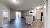 This single-floor residence offers a practical and well-organized layout designed for comfortable everyday living. The open-concept living and dining area serves as the heart of the space, featuring durable wood-style flooring that extends throughout the common areas. A peninsula-style kitchen sits at the center, equipped with white cabinetry, light countertops, a black gas range with overhead ventilation, and a black refrigerator. The kitchen flows seamlessly into the living area, which is brightened by a sliding glass door leading to a balcony, allowing natural light to fill the space.

The bedrooms are carpeted and generously proportioned, each featuring windows that invite natural light and views of the surrounding greenery. One bedroom includes direct access to a full bathroom with a tub and closet, providing added convenience. An additional bedroom offers a similarly spacious footprint with a window centered on the exterior wall.

The bathroom features a white vanity with a single sink, a mirror, and wood-style flooring consistent with the rest of the unit. Throughout the residence, textured ceilings and neutral-toned walls create a clean, understated aesthetic that provides a versatile backdrop for a variety of interior styles.
