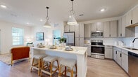 This thoughtfully designed 2-bedroom, 2-bathroom single-story residence offers a bright, open-concept layout with modern finishes throughout. The combined kitchen and living area serves as the heart of the home, featuring light wood-style flooring, recessed lighting, and large windows that invite natural light. The kitchen is equipped with stainless steel appliances, including a refrigerator, range, microwave, and dishwasher, complemented by light wood-grain cabinetry, crisp white quartz countertops, a clean tile backsplash, and a matte black faucet. A central island with seating provides additional prep space and casual dining. The living area flows seamlessly from the kitchen, offering a comfortable and airy atmosphere. Both bedrooms are carpeted and well-sized, with the primary bedroom featuring a ceiling fan, ample natural light through slatted blinds, and access to a walk-in closet with built-in shelving and hanging storage. The en-suite primary bathroom includes a double vanity with light wood cabinetry, a glass-enclosed shower, and wood-style flooring. A second well-proportioned bedroom is served by a second full bathroom. The unit is completed by a dedicated laundry room and two closets, offering practical storage throughout.