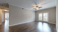This single-floor residence offers a cohesive and well-designed layout finished with rich, dark hardwood flooring that flows consistently throughout the space. The main living area is highlighted by elegant crown molding, a ceiling fan with a light fixture, and a set of French doors that invite natural light and provide access to the outdoors. The neutral gray walls create a clean, versatile backdrop throughout the home.

The kitchen is thoughtfully designed with dark cabinetry, granite-style countertops, and a full suite of appliances including a stainless steel refrigerator, microwave, and range. A breakfast bar peninsula connects the kitchen to the adjacent dining or living area, making it well-suited for both everyday meals and entertaining. A set of double doors within the kitchen provides additional storage or pantry space.

The bedrooms are generously sized, each featuring ceiling fans and large windows dressed with blinds that allow for natural light while maintaining privacy. One bedroom benefits from multiple windows arranged in a corner configuration, enhancing the sense of openness.

The bathroom is equipped with dark vanity cabinetry, a wide mirror, gray countertops, and hardwood-style flooring, maintaining the consistent design language found throughout the home. Overall, the space presents a polished, neutral aesthetic with quality finishes and functional, comfortable living areas.