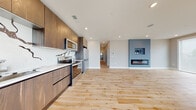 This single-floor space showcases a thoughtfully designed open-concept layout with light hardwood flooring running consistently throughout. The open living and kitchen area serves as the heart of the unit, anchored by a striking accent wall in muted blue that features a built-in media niche and a sleek linear fireplace, creating a contemporary focal point. Recessed lighting illuminates the space, complementing the natural light that filters in through large windows and a glass sliding door in one of the bedrooms, offering outdoor views.

The kitchen is outfitted with dark wood flat-panel cabinetry that extends to the ceiling, a bold marble-veined backsplash with dramatic black patterning, white countertops, and a full suite of stainless steel appliances including a French door refrigerator. A hallway connects the living areas to the private rooms and bathrooms, maintaining a clean and organized flow.

The bathrooms are finished to a high standard, featuring floor-to-ceiling marble-look tile in the walk-in glass-enclosed showers, wall-mounted vanities with integrated sinks, and mirrored medicine cabinets. The bedrooms are calm and understated, with neutral gray walls and the same warm hardwood flooring found throughout the rest of the space.
