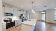 Located at 601 Gilcrest Farm Rd in Wake Forest, NC, this well-appointed single-story home offers three bedrooms, two bathrooms, and a thoughtfully designed layout across a generous footprint. The heart of the home is an open-concept kitchen and living area featuring warm hardwood-style flooring, recessed lighting, and elegant pendant lights above a large central island with a white quartz countertop and undermount sink. The kitchen is outfitted with gray shaker-style cabinetry, stainless steel appliances including a refrigerator with ice maker, electric range, and built-in microwave, complemented by a herringbone-patterned tile backsplash. A built-in desk nook adds functional versatility to the living area. The bedrooms are carpeted and bright, each featuring ceiling fans and windows that allow natural light to fill the rooms. The primary bedroom is generously sized and accompanied by a walk-in closet with wire shelving. The bathrooms are finished with gray vanities, quartz countertops, framed mirrors, and tub-shower combinations. A dedicated laundry room houses a full-size washer and dryer with overhead wire shelving for added storage. Three closets throughout the home ensure ample storage. The clean, neutral palette and modern design choices give this home a fresh and welcoming ambiance.