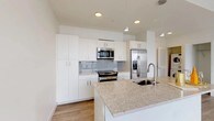 Located at 1011 Washington Blvd in Stamford, CT, this modern one-bedroom, one-bathroom residence delivers a clean, contemporary aesthetic across a thoughtfully designed single-floor layout. Light-toned hardwood-style flooring flows seamlessly throughout, complementing the bright white walls and creating a cohesive, airy atmosphere.

The open-concept kitchen is a standout feature, outfitted with white flat-panel cabinetry, granite countertops, a subway tile backsplash, and a full suite of stainless steel appliances including a range, built-in microwave, and french door refrigerator. A center island with an undermount sink adds both workspace and a natural gathering point.

The living area is bathed in natural light thanks to expansive floor-to-ceiling windows framed in dark metal, offering sweeping elevated views of the Stamford skyline and surrounding cityscape. The bedroom is generously proportioned, featuring its own access to a walk-in closet and direct connection to the main corridor.

The bathroom is finished with neutral large-format tile surrounding a soaking tub and shower combination, accented by chrome fixtures and recessed lighting. The overall design of this residence emphasizes modern simplicity, abundant natural light, and high-quality finishes, making it a refined urban living space in the heart of Stamford.