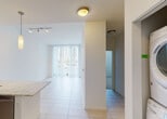 Located at 6055 NW 105th Ct in Doral, Florida, this single-floor residence offers a contemporary and well-appointed interior designed for comfortable living. The open-concept kitchen is a standout feature, showcasing dark flat-panel cabinetry, light granite countertops, and a full suite of stainless steel appliances including a French door refrigerator with ice and water dispenser, electric range, built-in microwave, and dishwasher. A peninsula with an undermount sink and elegant pendant lighting serves as a natural divider between the kitchen and the bright living area, which is finished with large-format tile flooring and floor-to-ceiling vertical blinds that allow for ample natural light. Track lighting throughout the main living spaces adds a modern, layered lighting scheme. A dedicated in-unit laundry area with a stacked washer and dryer provides added convenience. The bathroom features large-format white subway tile surrounding a full soaking tub and shower combination, complemented by brushed nickel fixtures and a granite-topped vanity. The spacious walk-in closet is carpeted and equipped with wire shelving and hanging rods, offering generous storage. The clean white walls and neutral palette throughout create a bright, airy ambiance that defines this well-designed Doral residence.