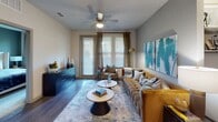 This single-floor residence showcases a thoughtfully designed layout with modern finishes and a cohesive contemporary aesthetic. The kitchen is a standout feature, equipped with stainless steel appliances including a range, microwave, dishwasher, and refrigerator. Warm-toned, wood-grain cabinetry extends to the ceiling, complemented by granite countertops, a tile backsplash, and a kitchen island with bar seating — ideal for casual dining or entertaining.

The living area offers a comfortable, open feel with wood-style flooring, a ceiling fan, and large windows that admit generous natural light. A door provides access to an outdoor area, further enhancing the sense of openness. Bold teal artwork and warm gold accents create a cohesive modern design throughout the space.

The two bedrooms are carpeted for comfort, each featuring windows with blinds and curtains that allow for natural light while maintaining privacy. One bedroom includes an accent wall in deep teal, adding a stylish focal point.

Two full bathrooms serve the residence. One features a tub-shower combination with tile surround, wood-style flooring, and open shelving. The second bathroom includes a granite-topped vanity and wood-style flooring, accented by coordinating décor.