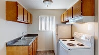 This single-floor unit offers a practical and straightforward layout designed for efficient use of space. The galley-style kitchen is lined with warm oak cabinetry on both sides, providing ample upper and lower storage. Dark granite-look countertops complement the cabinetry, while a stainless steel sink sits beneath a window fitted with vertical blinds. White appliances, including a coil-burner electric range with an overhead exhaust hood and a full-size refrigerator, complete the kitchen. Wood-look vinyl plank flooring runs throughout the kitchen and entry areas.

The living area transitions to neutral carpet and features a ceiling fan, a built-in closet with shelving, and baseboard heating units along the walls. A front entry door with a sidelight panel allows natural light in and provides views of surrounding greenery. The bedroom is a calm, carpeted space with a window dressed in vertical blinds and its own baseboard heater. The bathroom includes a full-size soaking tub and shower combination, finished with clean white square tile surround and chrome fixtures. The overall aesthetic is clean and functional, with neutral tones throughout.
