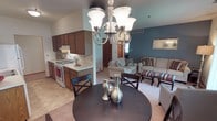 This single-floor residence offers a thoughtfully designed layout that balances comfort and functionality. The open-concept living and dining area serves as the heart of the home, where a bold teal accent wall provides a striking backdrop for the carpeted living room. A sliding glass door with vertical blinds leads to an outdoor balcony, allowing natural light to fill the space. The dining area is defined by a brushed nickel chandelier suspended over a round dark wood table, accompanied by a window overlooking greenery outside.

The galley-style kitchen is efficiently arranged with warm wood cabinetry lining both sides, white appliances including a gas range and full-size refrigerator, a double basin sink, and ample counter space. The kitchen opens conveniently toward the main living area.

The primary bedroom features plush carpeting, a mirrored sliding closet door revealing a well-organized walk-in closet, and an en-suite bath access. A second bedroom, equally comfortable, also offers a mirrored sliding closet, carpeted flooring, and a window with outdoor views. Both bedrooms provide a calm, neutral atmosphere well-suited for rest. Throughout the residence, warm wood trim accents and consistent flooring choices create a cohesive, inviting aesthetic.
