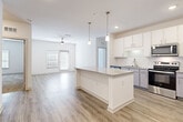 This well-appointed single-floor residence offers a bright, contemporary design throughout. The open-concept kitchen is a standout feature, showcasing white shaker cabinetry, granite countertops, a white subway tile backsplash, and a full suite of stainless steel appliances, including a French door refrigerator, electric range, microwave, and dishwasher. A large central island with a granite surface and pendant lighting above anchors the space, flowing seamlessly into the living area, which features light wood-look flooring, a ceiling fan, and access to an exterior door that invites natural light. The bedrooms are carpeted and generously sized, each equipped with ceiling fans and ample closet space — including a spacious walk-in closet with wire shelving. The primary en suite bathroom features dual granite-topped sinks, modern brushed nickel fixtures, a glass-enclosed shower, and wood-look flooring. A dedicated in-unit laundry room accommodates a full-size washer and dryer with additional wire shelving for storage. Throughout the residence, recessed lighting, clean white walls, and consistent finishes create a cohesive and functional living environment.