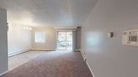 This single-floor space is designed with a practical, open layout that maximizes livability across its key areas. The living room serves as the central gathering space, finished with plush wall-to-wall carpeting in a warm neutral tone and painted in soft gray hues. A sliding glass door opens directly onto a private balcony, allowing natural light to fill the room while providing outdoor views of the surrounding neighborhood. A secondary window on the adjacent wall further brightens the space. Baseboard heating units line the walls, ensuring efficient climate control throughout. A textured popcorn ceiling adds a classic character overhead.

A transition from carpet to tile flooring marks the entry into the dining area, which is accented by a chandelier and connects seamlessly to the kitchen. The kitchen is outfitted with white cabinetry, dark laminate countertops, a stainless steel sink, a coil-element range with overhead ventilation, and durable tile flooring, providing a clean and functional workspace.

The bedroom is generously proportioned, featuring carpet, a wide window with blinds, and baseboard heating. The bathroom offers a full-size soaking tub with a shower, a white vanity, tile flooring, and a bright, clean finish throughout.