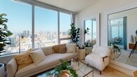 Located on a high floor at 1475 Island Ave in San Diego, this model unit showcases a thoughtfully designed single-level layout that blends modern aesthetics with comfortable urban living. Light-toned tile flooring flows through the entryway and into the main living areas, creating a seamless and airy feel throughout.

The open-concept living area is a true highlight, anchored by expansive floor-to-ceiling windows that frame sweeping panoramic views of the San Diego skyline and bay. Natural light floods the space throughout the day, enhancing the bright, minimalist atmosphere.

The kitchen is well-appointed with sleek white cabinetry extending to the ceiling, stainless steel appliances including a refrigerator, range, and microwave, a generous island with an undermount sink and quartz-style countertops, and recessed lighting overhead.

The bedroom is an inviting retreat featuring plush carpeting, a mirrored sliding closet, and a window that captures city views. A statement gold chandelier adds an elegant touch, complementing the warm, layered décor.

The bathroom is finished in a clean, neutral palette with tile flooring, a white vanity with ample cabinetry, a large mirror, and a shower/tub combo. A built-in linen closet adds practical storage. Overall, the unit exudes a calm, contemporary ambiance ideal for sophisticated city living.