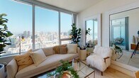Located on a high floor at 1475 Island Ave in San Diego, this model unit showcases a thoughtfully designed single-level layout that blends modern aesthetics with comfortable urban living. Light-toned tile flooring flows through the entryway and into the main living areas, creating a seamless and airy feel throughout.

The open-concept living area is a true highlight, anchored by expansive floor-to-ceiling windows that frame sweeping panoramic views of the San Diego skyline and bay. Natural light floods the space throughout the day, enhancing the bright, minimalist atmosphere.

The kitchen is well-appointed with sleek white cabinetry extending to the ceiling, stainless steel appliances including a refrigerator, range, and microwave, a generous island with an undermount sink and quartz-style countertops, and recessed lighting overhead.

The bedroom is an inviting retreat featuring plush carpeting, a mirrored sliding closet, and a window that captures city views. A statement gold chandelier adds an elegant touch, complementing the warm, layered décor.

The bathroom is finished in a clean, neutral palette with tile flooring, a white vanity with ample cabinetry, a large mirror, and a shower/tub combo. A built-in linen closet adds practical storage. Overall, the unit exudes a calm, contemporary ambiance ideal for sophisticated city living.