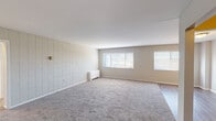 This single-floor unit offers a well-organized layout with distinct living, sleeping, kitchen, and bathroom areas. The living room is generously proportioned, featuring soft wall-to-wall carpeting, distinctive vertical white wood paneling on one wall, and multiple windows that allow natural light to fill the space. A baseboard heating unit ensures year-round comfort. Transitioning into the kitchen, the space is equipped with crisp white shaker-style cabinetry reaching to the ceiling, granite-look countertops, a stainless steel sink, and a black gas range. An adjacent folding-door pantry provides additional storage with built-in shelving. The bedroom is well-sized with plush carpeting, neutral toned walls, and a built-in closet offering ample storage. A second door from the bedroom provides convenient access to adjacent areas. The bathroom is clean and functional, featuring a combination tub and shower with tiled surround, a single-sink vanity with wood cabinetry, and a window above the tub for natural ventilation and light. Throughout the unit, hard-surface flooring in the entry and kitchen transitions seamlessly to carpet in the living and sleeping areas, creating a cohesive and practical interior.