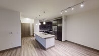 This single-floor residence in Grand Prairie, Texas offers a thoughtfully designed open-concept layout that seamlessly connects the kitchen, dining, and living areas. The kitchen serves as the focal point of the main living space, showcasing rich dark cabinetry, a grey subway tile backsplash, granite countertops, and a full suite of stainless steel appliances including a French door refrigerator, range, and built-in microwave. A central island with an undermount sink and pendant lighting above provides additional workspace and casual seating. Track lighting throughout the main area ensures well-lit functionality. Light wood-tone laminate flooring runs throughout the open living spaces, complemented by neutral walls and dark baseboards that create a modern, cohesive aesthetic. The spacious living area features a ceiling fan and flows naturally from the kitchen. The bedroom wing includes carpeted rooms with natural light provided by window blinds. Two bathrooms are finished with granite-topped dark vanities and large mirrors. The primary bath features a soaking tub with tiled surround and a double-sink vanity, while a secondary bath offers a frameless glass walk-in shower with large-format tile. The overall design balances contemporary finishes with functional, comfortable living.