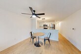 Located in Seattle's vibrant University District, this 1-bedroom, 1-bathroom unit offers a well-designed layout across a single floor. Light wood flooring runs throughout, lending warmth and continuity to every room.

The open-concept kitchen and living area serves as the heart of the unit. The kitchen features white upper cabinetry, gray lower cabinets, a white subway tile backsplash, stainless steel appliances including a refrigerator, electric range, and microwave, plus a peninsula with a white countertop and pendant lighting above. A ceiling fan with integrated lighting anchors the combined living and dining space. The living area opens to a balcony through large sliding glass doors framed by vertical blinds, offering views of surrounding greenery.

The bedroom is a bright, comfortable retreat with two windows overlooking lush tree canopy, a ceiling fan, and light-filled ambiance. An additional den provides flexible space for a home office or secondary sleeping area. Three closets offer generous storage throughout the unit.

The bathroom features a full soaking tub and shower combo, a vanity, and matte black fixtures that add a modern touch. A clean, minimalist hallway connects all rooms efficiently. The entry features a crisp white paneled door completing this well-appointed urban residence.