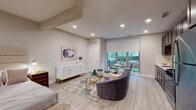 Located at 59 2nd Ave in Raritan, NJ, this thoughtfully designed single-floor residence offers a seamless blend of modern aesthetics and functional living. The open-concept layout connects the living, dining, and sleeping areas, creating an airy and cohesive environment throughout.

The living area is anchored by light hardwood-style flooring, recessed lighting, and a large window with a roller shade that floods the space with natural light and provides views of the surrounding greenery. A plush seating arrangement, glass coffee table, and elegant white sideboard with gold accents add refined character to the room.

The sleeping area is generously proportioned, featuring a full-sized bed with an upholstered headboard, a bedside chest, and ample closet space. The room maintains the same warm, neutral palette found throughout the residence.

The kitchen is well-appointed with rich dark cabinetry, stainless steel appliances including a gas range, microwave, refrigerator, and dishwasher, and clean white countertops. A window adjacent to the kitchen allows for additional natural light.

The bathroom features a full tub-shower combination with mosaic tile surround, a dark wood vanity with a white basin, a large mirror, and neutral tile flooring, completing this polished and practical space.