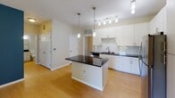 This single-floor residence offers a thoughtfully designed layout that balances modern finishes with everyday functionality. The kitchen serves as a centerpiece of the home, showcasing crisp white cabinetry, dark granite countertops, and a full suite of stainless steel appliances including a range, microwave, refrigerator, and dishwasher. A subway tile backsplash adds a clean, contemporary touch, while a central island provides additional prep and counter space. Pendant lighting and a track light fixture illuminate the kitchen with a warm, practical glow. Light-toned hardwood-style flooring flows throughout the main living and kitchen areas, lending a bright and cohesive feel to the space. The bathroom is well-appointed with a full soaking tub and shower combination, accented by classic white and neutral tile work, a dark granite vanity countertop, and white cabinetry for storage. The bedrooms feature plush wall-to-wall carpet and generously sized windows dressed with horizontal blinds, allowing natural light to filter in while maintaining privacy. One bedroom includes built-in shelving, adding practical storage. Overall, the residence presents a clean, modern aesthetic with consistent finishes throughout, creating a comfortable and functional living environment.