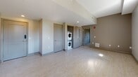 Located in the heart of downtown Rochester, New York, this single-floor unit at 183 E Main St offers a thoughtfully designed layout with modern finishes throughout. The open living area features light luxury vinyl plank flooring, neutral gray walls, and a coffered ceiling detail that adds architectural interest while natural light filters in through well-positioned windows. The contemporary kitchen is a standout feature, equipped with stainless steel appliances including a range, built-in microwave, and dishwasher. Dark wood-grain cabinetry pairs elegantly with crisp white countertops and a glossy gray subway tile backsplash, creating a sleek, functional workspace with ample storage. The bathroom is clean and efficiently designed, featuring a combination soaking tub and shower with a handheld fixture, brushed nickel hardware, and a vanity with warm wood-toned cabinetry set against light flooring. A dedicated laundry area includes a stacked washer and dryer unit, providing added convenience. Additional interior doors suggest flexible use of space, accommodating storage or multi-purpose rooms. The overall aesthetic is contemporary and cohesive, with a neutral palette and quality finishes that create a comfortable, move-in-ready environment.