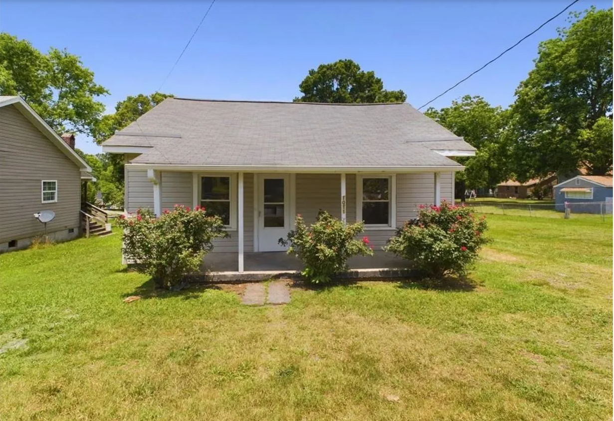 Front Exterior: A cozy covered porch surrounded by vibrant landscaping with blooming rose bushes. - 1011 Elm St