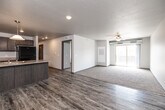 Located at 1360 NE Primrose Ln in Grimes, Iowa, this well-appointed three-bedroom, two-bathroom single-floor residence offers a thoughtfully designed layout with modern finishes throughout. The open-concept kitchen and living area serves as the heart of the home, featuring wood-look luxury vinyl plank flooring, a large center island with a double sink and pendant lighting, dark taupe cabinetry, light countertops, and black appliances including a refrigerator, range, and built-in microwave. A sliding glass door in the living area leads to a private balcony, while a ceiling fan and plush carpeting add comfort to the space. A dedicated pantry provides additional kitchen storage. The three bedrooms are carpeted and each includes closet space, with the primary bedroom offering a generously sized layout. Five closets total ensure ample storage throughout the unit. The two bathrooms feature wood-look vinyl plank flooring, dark vanity cabinetry, and light stone-finish countertops; one includes a full soaking tub. A dedicated laundry room adds everyday convenience. A central hallway connects all rooms efficiently, and exposed ductwork in select areas lends a subtle industrial character to the otherwise clean, neutral aesthetic.