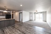 Located at 1360 NE Primrose Ln in Grimes, Iowa, this well-appointed three-bedroom, two-bathroom single-floor residence offers a thoughtfully designed layout with modern finishes throughout. The open-concept kitchen and living area serves as the heart of the home, featuring wood-look luxury vinyl plank flooring, a large center island with a double sink and pendant lighting, dark taupe cabinetry, light countertops, and black appliances including a refrigerator, range, and built-in microwave. A sliding glass door in the living area leads to a private balcony, while a ceiling fan and plush carpeting add comfort to the space. A dedicated pantry provides additional kitchen storage. The three bedrooms are carpeted and each includes closet space, with the primary bedroom offering a generously sized layout. Five closets total ensure ample storage throughout the unit. The two bathrooms feature wood-look vinyl plank flooring, dark vanity cabinetry, and light stone-finish countertops; one includes a full soaking tub. A dedicated laundry room adds everyday convenience. A central hallway connects all rooms efficiently, and exposed ductwork in select areas lends a subtle industrial character to the otherwise clean, neutral aesthetic.