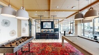 This thoughtfully designed single-floor amenity space combines contemporary aesthetics with a welcoming, social atmosphere. The lobby greets visitors with large-format tile flooring, an eye-catching orange sofa, bold wall art, and a sculptural white lattice installation, setting an upscale tone throughout. Floor-to-ceiling windows flood the space with natural light and offer direct views of the lush outdoor courtyard and pool area beyond.

The game room serves as a vibrant social hub, anchored by a pool table and foosball table set atop a rich, jewel-toned red area rug. Oversized pendant lights hang above, while intricate floral line-art murals adorn the white walls. A large flat-screen TV adds an entertainment focal point to the room.

Adjacent to the game room, a sophisticated lounge and bar area features a striking marble-topped island with seating, custom blue cabinetry with under-counter refrigeration, decorative pendant lighting, and a mounted television. This space flows seamlessly into a dining area with a solid wood communal table and steel-framed glass partitions that define zones without sacrificing openness.

Warm wood ceiling panels with structural beam detailing carry throughout, lending a cohesive and refined character to every area of this exceptional amenity floor.