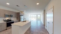 This single-floor unit is designed with a clean, contemporary aesthetic and a practical open-concept layout. The kitchen serves as a central hub, featuring a large island with a double-basin sink, white quartz countertops, light wood-toned cabinetry extending to the ceiling, and a full suite of stainless steel appliances including a refrigerator, range, and microwave. Pendant and recessed lighting illuminate the space, which flows seamlessly into a spacious living area with large windows that draw in abundant natural light and offer outdoor views of the surrounding landscape.

The bedrooms are carpeted and well-proportioned, each with ample closet space and windows providing views and ventilation. The primary bathroom includes a dual-sink vanity with wood-toned cabinetry, a large mirror, built-in wall shelving, and a separate shower. The secondary bathroom features a combined tub and shower, a single vanity, and matching finishes. A dedicated in-unit laundry area houses a full-size front-loading washer and dryer with overhead wire shelving. Throughout, neutral tones, tile flooring in common areas, and recessed lighting create a cohesive and functional living environment.