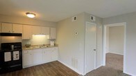 Located at 250 Sage Ave. in Mobile, Alabama, this single-floor space offers a practical and well-maintained layout designed for comfortable everyday living. The kitchen is outfitted with clean white cabinetry, a double-basin sink, and granite-look countertops that provide ample prep space. Under-cabinet lighting adds both functionality and a warm ambiance to the cooking area. The flooring transitions from rich hardwood-style planks in the kitchen and main living areas to carpet in the adjacent spaces, adding textural variety throughout the unit. Neutral, warm-toned walls create a bright and welcoming atmosphere, while the white trim and doors provide a crisp, finished look. The space is equipped with ceiling-mounted HVAC vents and a programmable thermostat, ensuring year-round climate control. A floor-level heating vent is also present, offering additional warmth during cooler months. The doors leading off the main area suggest thoughtfully separated living zones, providing privacy and organization within the single-floor footprint. Overall, the space presents a clean, move-in-ready environment with functional finishes suited to a variety of lifestyles.