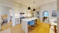 This thoughtfully designed two-bedroom, two-bathroom residence in California offers a well-appointed single-level layout that maximizes every square foot. Light hardwood flooring flows throughout, complementing a clean, modern aesthetic anchored by crisp white walls and warm natural wood accents.

The open-concept kitchen and dining area is a standout feature, showcasing two-tone cabinetry — upper white panels paired with light wood lower cabinets — stainless steel appliances, a large center island with seating, pendant lighting, and under-cabinet illumination. A stacked in-unit washer and dryer is conveniently integrated nearby. The dining area benefits from generous natural light through floor-to-ceiling sheer-draped windows.

The living room continues the bright, airy feel with large windows offering outdoor views and access to a private balcony. A versatile den adds additional flexible living space. The primary bedroom is a serene retreat finished in soft neutral tones, while the second bedroom features ample natural light and a large window. Both bathrooms are finished with clean white subway tile — one featuring a glass-enclosed walk-in shower with matte black fixtures, the other a full soaking tub. Three closets and a dedicated entrance complete this well-organized home.