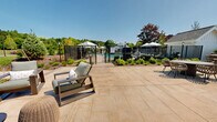 Located at 580 Main St in Bolton, Massachusetts, this thoughtfully designed outdoor community space offers a welcoming and resort-like environment set against a lush New England landscape. The grounds are meticulously maintained, featuring expansive manicured lawns, ornamental plantings, and mature trees that provide a natural, serene atmosphere throughout.

A central feature of the property is a generously sized outdoor swimming pool, encircled by a spacious pool deck furnished with lounge chairs and market umbrellas, ideal for relaxation and recreation. The pool area is fenced for safety and framed by a backdrop of tall, dense trees that enhance the sense of privacy and tranquility.

Paved walkways wind through the property, connecting key areas including an outdoor patio and social gathering space outfitted with durable seating, tables, and pergola-style structures. Carefully curated landscaping beds line the pathways, adding seasonal color and visual interest throughout the grounds.

The overall layout of the campus is thoughtfully organized, with white clapboard-style structures that reflect a classic New England architectural character. The single-story design ensures accessibility across the entire property. Ample open green space provides room for leisure and outdoor activities, while stylish lighting fixtures and well-maintained hardscape elements contribute to an inviting, community-centered ambiance.
