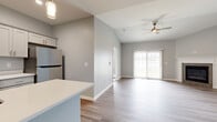 Located at Captains Quarter in North Tonawanda, NY, this single-floor residence offers a thoughtfully designed open-concept layout finished with consistent neutral gray tones and wood-look flooring throughout the main living areas. The kitchen is outfitted with white shaker-style cabinetry, quartz countertops, stainless steel appliances including a gas range, built-in microwave, and refrigerator, complemented by a central island that provides additional prep and serving space. The kitchen flows directly into the living area, which features vaulted ceilings, a ceiling fan, and a tile-surround fireplace with a white mantle. Sliding glass doors bathe the living space in natural light and provide access to the outdoors. The bedroom is carpeted for comfort and includes a generous walk-in closet with wire shelving systems. The bathroom is well-appointed with a framed glass walk-in shower, white vanity cabinetry with quartz countertops, gold hardware accents, and wood-look flooring. Additional highlights include an in-unit laundry area and an attached single-car garage with an automatic opener, providing convenient and secure parking and storage.