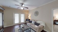 This single-floor, 2-bedroom, 2-bathroom residence is thoughtfully designed to maximize both comfort and functionality. The living room serves as the heart of the home, featuring dark hardwood-style flooring, crown molding, a ceiling fan, and French doors that open to an outdoor area, allowing natural light to fill the space. Adjacent to the living room is a dedicated dining area, also adorned with crown molding and dark hardwood flooring, providing an intimate setting for meals. The kitchen is well-appointed with rich dark wood cabinetry, granite-style countertops, stainless steel appliances — including a range, microwave, and dishwasher — and durable hardwood-style flooring. A built-in desk nook with overhead cabinetry near the entryway offers a convenient workspace. Both bedrooms are carpeted and equipped with ceiling fans, offering a comfortable and quiet retreat. Each bedroom features generous closet space. The two bathrooms include vanities with large mirrors and ample counter space. Neutral, warm tones are carried consistently throughout the home, creating a cohesive and inviting ambiance from room to room.