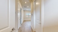 This single-story home presents a clean, contemporary design characterized by neutral tones, light wood-look luxury vinyl plank flooring, and crisp white trim throughout. The open-concept kitchen and living area serves as the central hub of the home, featuring white shaker-style cabinetry, stainless steel appliances including a refrigerator, range, microwave, and dishwasher, and a central island with pendant lighting overhead. A ceiling fan adds comfort to this shared living space.

A well-proportioned hallway connects the home's various rooms, lined with recessed lighting and fitted with a ceiling-mounted attic access panel. Multiple bedrooms are accessible from this corridor, each finished with the same wood-look flooring, neutral walls, ceiling fans with light fixtures, and windows fitted with blinds that allow for natural light and outdoor views of the surrounding neighborhood.

The primary bathroom features a long vanity with white cabinetry and light countertops, a framed walk-in glass shower with tiled walls and a built-in niche, and a separate water closet. An adjacent walk-in closet with a window provides generous storage. The overall ambiance of the home is bright, clean, and move-in ready.