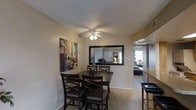 This single-floor residence offers a comfortable and cohesive living environment thoughtfully arranged across its main areas. The living room is a welcoming retreat, featuring plush carpeting, a textured ceiling, and a window dressed with layered blinds and dark curtains that allow for flexible light control. Decorative wall art and an eclectic mix of patterned furnishings lend the space a warm, personalized character.

Adjacent to the living room, the dining area provides a functional yet stylish setting for everyday meals and gatherings. A dark wood dining table with matching cross-back chairs anchors the space, while a large framed mirror on the wall adds depth and reflects light throughout the room. A ceiling fan overhead ensures comfortable airflow, and bold artwork featuring a Parisian cityscape adds a touch of cosmopolitan flair.

An open pass-through connects the dining area to the kitchen, enhancing the sense of flow between spaces. Soft carpeting continues throughout, contributing to the overall warmth of the interior. The layout is practical and well-proportioned, making efficient use of the available space while maintaining a cohesive, inviting ambiance throughout.