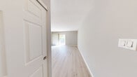 Located at 201 Idlewild Rd in Bel Air, Maryland, this single-floor unit offers a practical and efficient layout across two living areas and one full bathroom. Light wood-style flooring runs throughout the space, lending a clean, modern aesthetic that brightens each room.

The main living area is open and inviting, anchored by a sliding glass door fitted with vertical blinds that allow natural light to pour in while offering views of the surrounding greenery. This space connects seamlessly to a semi-open kitchen, which features warm-toned wood cabinetry, a pass-through counter, a range, and a sink — creating a functional cooking and dining zone that remains visually connected to the main living area.

The secondary living area, which can serve as a bedroom or flex space, includes a window with horizontal blinds that frame outdoor foliage, along with a wall-mounted air conditioning unit for climate control. Neutral gray walls throughout the unit provide a versatile backdrop adaptable to a variety of interior styles.

The bathroom is finished with classic white subway tile surrounding a full-size soaking tub and shower combination, complemented by clean chrome fixtures and consistent light flooring. White baseboards and trim throughout the unit add a crisp finishing touch, while the overall layout maximizes the efficient use of the available space.