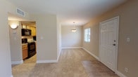 Located on Eden Isle Boulevard in Saint Petersburg, Florida, this single-floor residence offers a thoughtfully laid-out interior with a warm, neutral color palette throughout. The entry foyer features tile flooring that transitions into soft carpeting across the main living and dining areas. A pendant light fixture anchors the dining space, which flows openly into the living room — both bathed in natural light from windows fitted with blinds. Ceiling fans are present in the living areas and bedrooms, providing comfortable ventilation year-round. The galley-style kitchen is well-appointed with warm wood cabinetry, granite-look countertops, tile flooring, and black appliances including a refrigerator, range, microwave, and dishwasher. A dedicated bedroom features a ceiling fan, a window with outdoor views, and a reach-in closet with built-in shelving. Sliding glass doors in another room open directly to an outdoor balcony, offering views of the surrounding area. Both bathrooms are finished with tile flooring, wood vanity cabinetry, granite-look countertops, and large mirrors. The consistent warm-toned walls and clean white trim create a cohesive, inviting atmosphere throughout the entire space.
