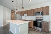 Located at 5577 Odana Rd in Madison, WI, this modern single-floor residence offers three bedrooms, two bathrooms, and four closets within a well-organized, open layout. The interior is defined by polished concrete floors that run throughout, lending an industrial-chic aesthetic that pairs seamlessly with clean white walls and crisp trim.

The kitchen and living area form the heart of the home, featuring warm wood-tone cabinetry, a white geometric tile backsplash, stainless steel appliances, and a center island topped with a light quartz surface. Stylish pendant lights hang above the island, enhancing both function and ambiance. Large windows allow ample natural light to fill the space, with views of the surrounding greenery and neighborhood.

The bedrooms offer bright, sun-drenched spaces with generous windows fitted with blinds. The primary bedroom stands out with a bold accent wall and sliding barn doors that add a modern, space-savvy touch, complemented by a ceiling fan for comfort. Each bathroom is finished with quartz countertops, wood-grain vanities, and full-size tub/shower combinations. A clean, well-lit hallway with warm wood built-in cabinetry connects the rooms efficiently. A private balcony provides outdoor access with open views of the surrounding area.