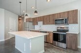 Located at 5577 Odana Rd in Madison, WI, this modern single-floor residence offers three bedrooms, two bathrooms, and four closets within a well-organized, open layout. The interior is defined by polished concrete floors that run throughout, lending an industrial-chic aesthetic that pairs seamlessly with clean white walls and crisp trim.

The kitchen and living area form the heart of the home, featuring warm wood-tone cabinetry, a white geometric tile backsplash, stainless steel appliances, and a center island topped with a light quartz surface. Stylish pendant lights hang above the island, enhancing both function and ambiance. Large windows allow ample natural light to fill the space, with views of the surrounding greenery and neighborhood.

The bedrooms offer bright, sun-drenched spaces with generous windows fitted with blinds. The primary bedroom stands out with a bold accent wall and sliding barn doors that add a modern, space-savvy touch, complemented by a ceiling fan for comfort. Each bathroom is finished with quartz countertops, wood-grain vanities, and full-size tub/shower combinations. A clean, well-lit hallway with warm wood built-in cabinetry connects the rooms efficiently. A private balcony provides outdoor access with open views of the surrounding area.