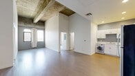 Located on Wilshire Boulevard in Los Angeles, this 2-bedroom, 2-bathroom loft-style residence combines industrial character with modern finishes across a single, well-configured floor. The open living area makes a strong architectural statement with soaring ceilings and dramatic exposed concrete beams overhead, creating a loft ambiance that sets this space apart. Light-toned hardwood-style flooring runs throughout the main living area, complementing the clean white walls and generous natural light that filters in through arched windows framed by simple white curtains.

The kitchen is efficiently designed with white cabinetry, white countertops, stainless steel appliances including a gas range, microwave, dishwasher, and refrigerator, along with an in-unit washer conveniently integrated into the layout. A hallway connects the main living space to the two bedrooms, both of which feature plush carpet flooring, arched windows with city views, and the same striking exposed concrete beam details found throughout the home.

The two bathrooms are finished in a clean, contemporary style — one featuring a full soaking tub with tiled surround, and the other offering a white vanity with stone-style countertops and mirrored medicine cabinets. The overall ambiance is urban and functional, with industrial design elements balanced by bright, neutral finishes.