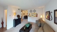This single-floor residence offers a comfortable and functional layout across several well-defined living spaces. The living room serves as the heart of the home, featuring plush carpeting, a textured ceiling, and a sliding glass door dressed with deep red curtains that provides access to an outdoor area and fills the room with natural light. A pass-through window connects the living room to the kitchen, creating an open sightline into the adjoining dining area, which is anchored by a ceiling fan and a full dining set. The galley-style kitchen is efficiently designed with warm wood cabinetry, laminate countertops, a double-basin sink, and white appliances including a range and refrigerator, all set above durable tile flooring. Two bedrooms offer carpeted floors and a relaxed ambiance; one features a walk-in closet, providing generous storage, while the other includes a window for natural light. The full bathroom is neatly appointed with a vanity, single-basin sink, toilet, and a tub-shower combination. Throughout the residence, neutral wall tones and textured ceilings create a cohesive, understated aesthetic suited for everyday living.