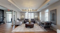 Located at 4170 Green Clover Dr in Hilliard, Ohio, this single-floor community clubhouse offers a refined and welcoming environment designed for both relaxation and social gatherings. The space is anchored by a grand great room showcasing a distinctive tray ceiling, decorative columns, and rich hardwood flooring that flows seamlessly throughout. A modern globe chandelier serves as a focal point, complementing the neutral gray palette and elegant crown molding that frame the room.

Abundant natural light pours in through multiple large windows fitted with plantation shutters, creating a bright and airy atmosphere. The lounge areas are thoughtfully arranged with comfortable seating configurations suited for both intimate conversations and larger group gatherings. A wall-mounted flat-screen TV and bar-height seating provide an entertainment-focused zone, ideal for communal viewing.

A dedicated kitchenette area features dark cabinetry, light countertops, a stainless steel sink with a professional-style faucet, and a coffee station, offering convenient refreshment amenities. French doors open to the exterior, further enhancing the connection between indoor and outdoor spaces. The overall ambiance is polished and contemporary, combining upscale architectural details with functional, community-oriented design.