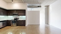 Located in the heart of Downtown Los Angeles on E 8th Street, this urban loft-style residence blends industrial character with contemporary design. Polished concrete floors run throughout the single-level layout, complemented by exposed concrete columns, visible ductwork, and a raw ceiling that together create a distinctive loft aesthetic. The open living area benefits from large industrial-style windows that flood the space with natural light and offer city views, enhancing the airy, open feel of the floor plan. The kitchen is well-appointed with dark espresso cabinetry, a subway tile backsplash, light countertops, and a full suite of stainless steel appliances including a refrigerator with ice maker, range, microwave, and dishwasher. Track lighting accents the kitchen and common areas. The spacious primary bedroom features polished concrete floors, generous natural light, and a sliding glass door. The bathroom is finished with large-format white floor tiles, a sleek floating vanity with gray countertop, a round mirror with wall sconces, and a combination tub and shower enclosed with glass sliding doors. The entryway features a steel-accented door alongside an electrical panel, adding to the unit's industrial character.