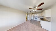 Located at 3300 Winterhaven St in Las Vegas, NV, this two-bedroom, two-bathroom unit offers a practical and well-appointed single-floor layout. The open living area features warm neutral-toned carpet and a ceiling fan with integrated lighting, flowing seamlessly into the kitchen. The kitchen is a standout feature, equipped with white shaker-style cabinetry, dark granite countertops, a classic subway tile backsplash, wood-look vinyl flooring, and white appliances including a refrigerator, electric range, microwave, and dishwasher. A track lighting fixture provides focused illumination over the workspace. A hallway connects the living area to both bedrooms and bathrooms. Each bedroom is carpeted and fitted with a ceiling fan, offering a comfortable and quiet retreat, with dedicated closets providing ample storage. The primary bedroom includes its own en-suite bathroom featuring a granite-topped vanity and a tub-shower combination. The second bathroom mirrors the same clean aesthetic with a granite vanity, wood-look tile flooring, and a tub-shower unit. Both bathrooms are finished with neutral tones and chrome hardware, contributing to the unit's cohesive, modern style throughout.
