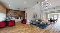 This contemporary community space boasts a spacious, open-concept layout with soaring ceilings and abundant natural light. The main area features a comfortable lounge with a tufted gray sofa, vibrant artwork, and a blue area rug. Adjacent is a dining area with a round table and red metal chairs, ideal for gatherings. A sleek kitchenette with white cabinetry and stainless steel appliances offers convenience. The space is enhanced by warm wood flooring throughout, creating a cohesive and inviting atmosphere. Large windows and glass doors provide views of an outdoor pool area, seamlessly connecting indoor and outdoor spaces.