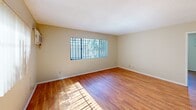 Located at 7050 Jordan Ave in the Canoga Park neighborhood of Los Angeles, this one-bedroom, one-bathroom unit is laid out efficiently across a single floor. Warm hardwood flooring runs throughout the space, creating a cohesive and inviting atmosphere from room to room.

The galley-style kitchen is lined with rich, warm-toned wood cabinetry on both sides, complemented by tile countertops and a white appliance suite including a gas range and microwave. A pass-through counter connects the kitchen to the open living and dining area, which receives generous natural light through a large picture window fitted with vertical blinds. A wall-mounted AC unit provides climate control in this area.

The bedroom offers a comfortable footprint with its own window for natural light and ventilation, a wall-mounted AC unit, and a mirrored sliding-door closet that adds depth and practicality to the room. The full bathroom includes a tub-and-shower combination with sliding glass doors, a single vanity with a marble-style countertop, and a mirror spanning the full width of the vanity. A clerestory window brings in natural light while maintaining privacy. The textured walls add a subtle architectural character to the bathroom. This unit offers a functional and straightforward layout well-suited for comfortable urban living in Los Angeles.