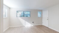 This well-appointed single-floor unit offers a clean, modern aesthetic across a thoughtfully laid-out floor plan. The main living area is bathed in natural light streaming through multiple windows fitted with horizontal blinds, casting warm patterns across the light-toned wood laminate flooring. Neutral wall tones and crisp white trim contribute to the bright, airy atmosphere throughout.

The kitchen stands out with a striking two-tone design, pairing bold navy blue lower cabinets with bright white upper cabinetry. A full suite of stainless steel appliances — including a refrigerator, range, and dishwasher — adds a polished, contemporary touch. A recessed ceiling light fixture provides focused illumination, and a window above the sink allows for additional natural light.

The bedrooms feature plush carpeting in a neutral tone, providing a comfortable and quiet retreat. One bedroom includes a sliding glass door dressed with vertical blinds, offering direct access to an outdoor area with views of surrounding greenery. Additional carpeted rooms share the same clean, minimalist character with ample wall space and good proportions.

The layout flows efficiently from the living and kitchen areas into the private rooms, making practical use of the available space. Overall, the unit presents a refreshed, move-in-ready condition with consistent finishes and a cohesive design sensibility throughout.