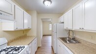 This single-floor, 2-bedroom, 1-bathroom unit offers a functional and efficiently arranged layout. The galley-style kitchen is a standout feature, lined on both sides with white shaker cabinetry and light granite-style countertops. White appliances, including a gas range and refrigerator, are integrated alongside a stainless steel sink, while wood-look flooring and a textured ceiling complete the space. The kitchen opens directly into a hallway connecting the remaining rooms.

The living room is generously proportioned, featuring wood-look flooring, baseboard heating, a wall-mounted air conditioning unit, and a sliding glass door fitted with vertical blinds that provides access to an outdoor area and brings in natural light with tree views.

Both bedrooms are carpeted and finished in neutral tones. The primary bedroom is notably spacious and features a window overlooking wooded surroundings, while the second bedroom offers comfortable proportions with convenient hallway access. A dedicated closet provides built-in shelving and a hanging rod for ample storage.

The bathroom includes a full tub-shower combination with panel surround. Throughout the unit, baseboard heating is consistently present, and the overall palette of warm whites and beige tones creates a clean, cohesive ambiance.
