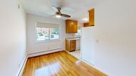 Located at 30 Charles River Rd in Waltham, Massachusetts, this two-bedroom, one-bathroom residence offers a practical and comfortable single-floor layout. Warm-toned hardwood flooring flows consistently throughout the living areas and bedrooms, lending a cohesive and inviting character to the entire space.

The combined kitchen and living area forms the heart of the home. The kitchen is equipped with warm wood cabinetry, ample upper and lower cabinet storage, white appliances including a refrigerator, electric range, built-in microwave, and dishwasher. The adjacent living area benefits from a ceiling fan and a window that overlooks the surrounding neighborhood, allowing natural light to brighten the room.

Both bedrooms are well-proportioned, featuring the same hardwood flooring, clean white walls, and baseboard heating. The primary bedroom offers a comfortable footprint, while the second bedroom provides flexible use as a guest room or home office. Each room includes a wall-mounted air conditioning unit for year-round comfort.

The bathroom is finished with classic white tile on both the walls and floor, and includes a full bathtub with shower, toilet, and vanity. The overall aesthetic throughout the residence is clean and straightforward, with a neutral palette that provides an excellent canvas for personalization.