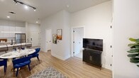 This contemporary 700 square foot apartment maximizes space with a thoughtful layout. The single bedroom, measuring 120 square feet, offers a serene retreat with large windows and decorative wall accents. The open-concept living area combines the kitchen and living room, creating a spacious feel. The kitchen boasts modern appliances, ample cabinetry, and a sleek design. A dedicated office space provides a functional work area, complete with built-in shelving and vibrant artwork. The bathroom features a wood vanity, large mirror, and glass-enclosed shower. Throughout the apartment, light wood flooring and white walls create a bright, airy ambiance. Large windows in every room flood the space with natural light, while sheer curtains offer privacy. The decor is a mix of modern and bohemian elements, with pops of blue and natural textures. Clever storage solutions and multi-functional furniture pieces maximize the efficiency of this compact yet stylish living space.