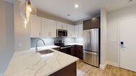 Located in Boston's Mission Hill neighborhood, this single-floor residence at 95 Saint Alphonsus Street offers a thoughtfully designed open-concept layout with modern finishes throughout. The kitchen is a standout feature, showcasing a two-tone cabinet design with crisp white upper cabinets and rich dark espresso lower cabinetry, complemented by quartz countertops with elegant veining and a light blue subway tile backsplash. Stainless steel appliances, including a refrigerator, electric range, and microwave, complete the space. A peninsula with pendant lighting provides additional prep space and casual seating, flowing seamlessly into the open living area. The living space is bright and airy, with light hardwood-style flooring and large corner windows that invite abundant natural light and offer views of the surrounding Boston streetscape. Recessed lighting throughout ensures a well-lit environment. The bathroom features large-format dark tile flooring, a dark wood vanity with a white countertop, a wide mirror, and clean white walls accented by chrome fixtures. A dedicated closet space and entry area round out the functional layout of this contemporary Boston residence.