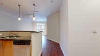 This thoughtfully designed single-floor residence offers a comfortable and cohesive living experience across a well-utilized footprint. The open-concept main area seamlessly connects the kitchen, dining, and living spaces, all unified by rich, warm-toned hardwood-style flooring and elegant crown molding throughout. Natural light flows in through a large window and glass door in the living room, which also features track lighting for added ambiance.

The kitchen is a functional highlight, boasting warm honey-toned cabinetry with ample storage, dark granite countertops, a tile backsplash, and a full suite of stainless steel appliances including a refrigerator, range, and built-in microwave. A peninsula countertop separates the kitchen from the living and dining areas, providing additional prep and seating space. The flooring transitions to large-format light tile within the kitchen.

The bedroom is a generously sized, carpeted retreat featuring a ceiling fan, direct access to the full bathroom, and an adjacent walk-in closet outfitted with multi-tiered wire shelving for organized storage. The bathroom is clean and well-appointed, featuring tile flooring, a combined tub and shower with tile surround, a toilet, and a vanity with dark countertops and warm wood cabinetry. An exterior entry door with a covered patio completes this well-rounded residence.